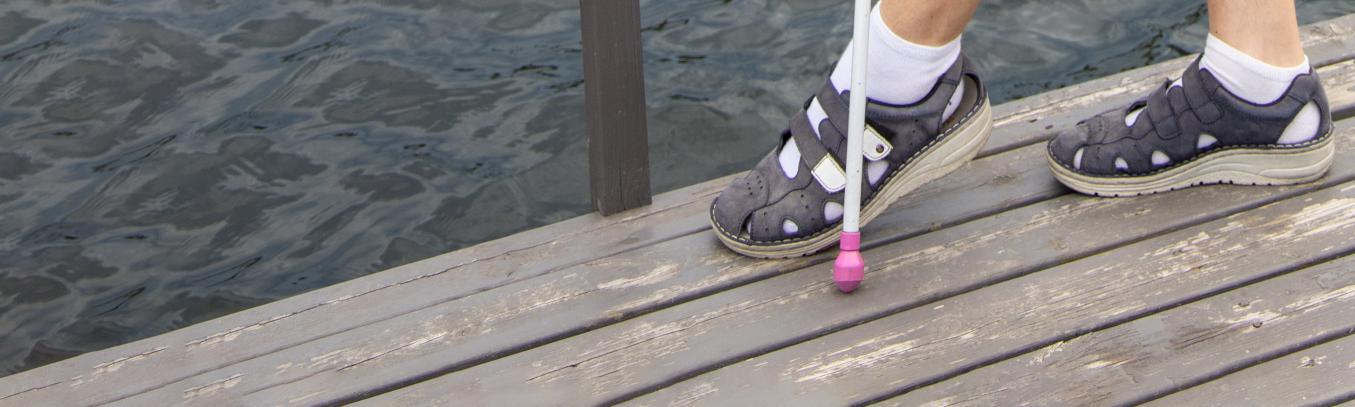 henkilö laiturilla josta näkyy vain kengät ja valkoinen keppi